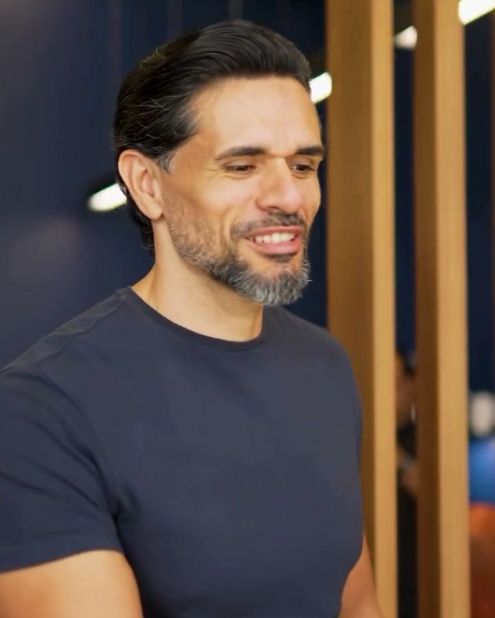 Barbeiro da Domen sorrindo diante da parede de madeira ripada